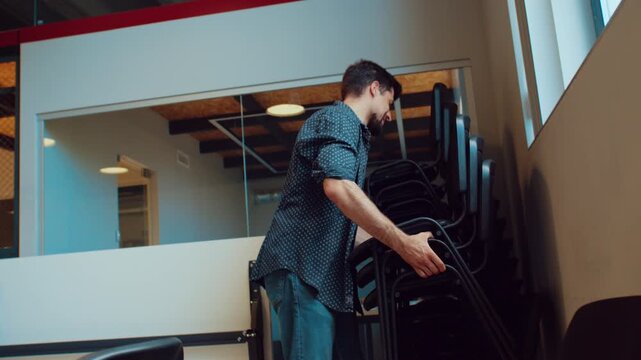 Man carries stacked chairs in modern office space during mid-morning hours