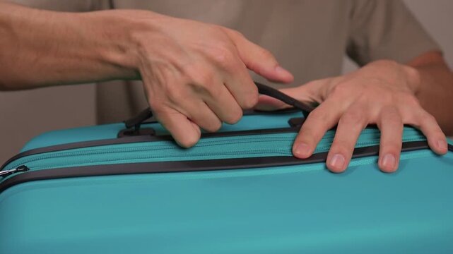 Traveler opening luggage, Close shot of hands unfastening suitcase zipper before travel, Detailed view of hands pulling zipper on vibrant teal travel case with anticipation