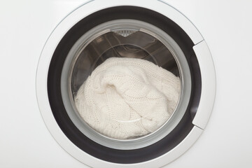 White soft sweater in closed washing machine. Closeup. Delicate knitted clothes care. Front view.