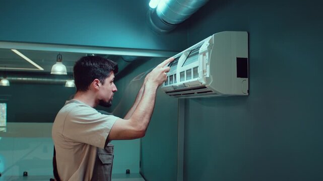 Worker installs air conditioning unit on the wall inside a modern office building
