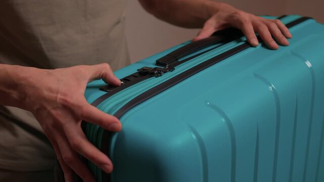 Secure suitcase with combo lock, Hands set combination on teal suitcase with textured surface, Closeup of hands adjusting numeric lock on stylish teal travel suitcase
