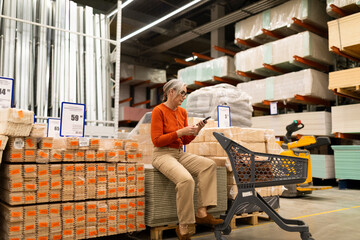 Woman sitting on stacked wood materials while using a smartphone in a hardware store during daytime shopping