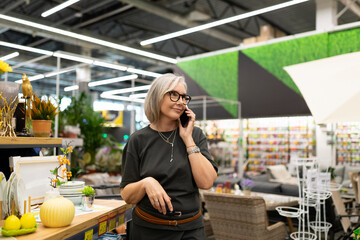 Woman talking on phone in home decor store while shopping for interior items during a bright day in a bustling retail environment