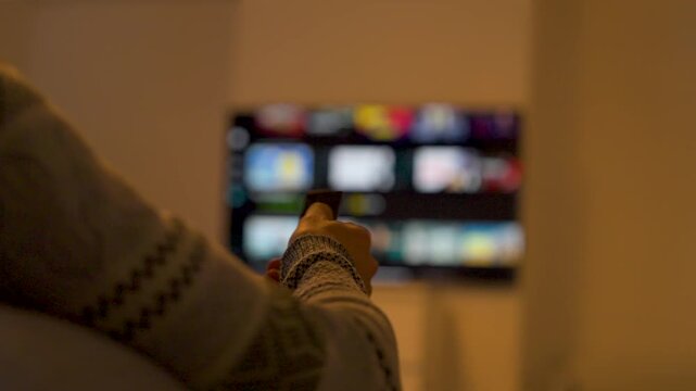 Person Using Remote Control Watching Blurred Tv at Home