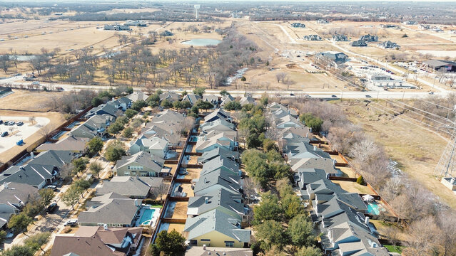 Neighborhood south of FM 407 transitions toward rural fields and utility corridors, water tower. Repeating roofs, fenced yards, pale grass, upscale suburban edges in Lantana, suburbs Dallas, TX