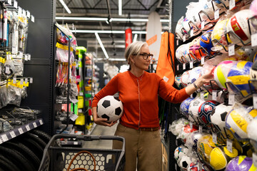 Woman shopping for sports equipment and holding a soccer ball in a sporting goods store during the day © Ivan Traimak