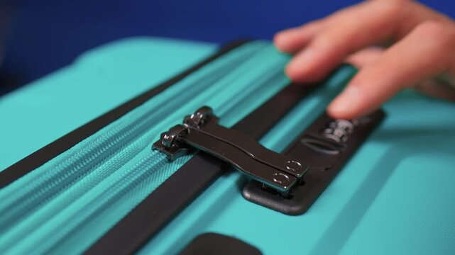 Secure suitcase with combo lock, Hands set combination on teal suitcase with textured surface, Closeup of hands adjusting numeric lock on stylish teal travel suitcase
