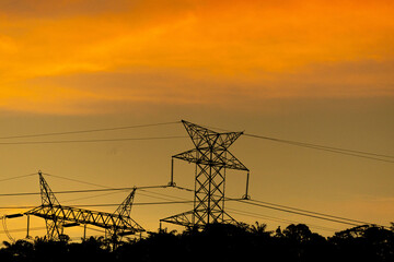 Uma torre de energia el&eacute;trica ou de transmiss&atilde;o uma estrutura met&aacute;lica com por-do-sol ao fundo. 