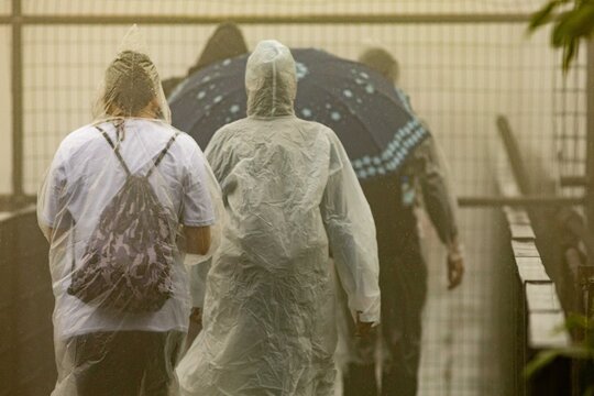 Pessoas vestidas com capa de chuva e guarda chuva em um dia chuvoso. 