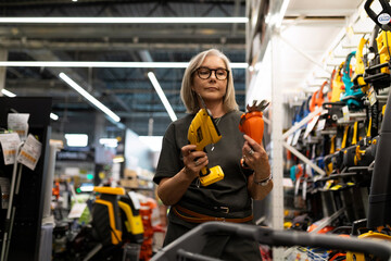 Woman shopping for tools in a hardware store while holding a glue gun and a decorative flower