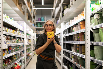 Woman holds a yellow decorative pot in a store aisle filled with gardening supplies and pots