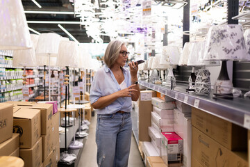 Woman shopping for lamps in a home goods store while using a smartphone to check details