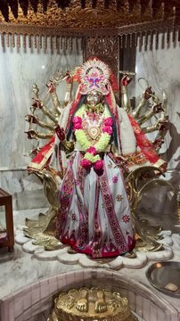 Goddess Durga adorned with vibrant floral garlands and traditional attire, depicted with multiple arms symbolizing power, protection, and divine feminine strength inside a temple setting.