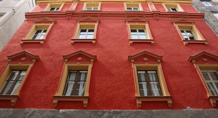 Obraz premium Red building exterior, eight windows with ornate gold frames, on a narrow street, viewed from below