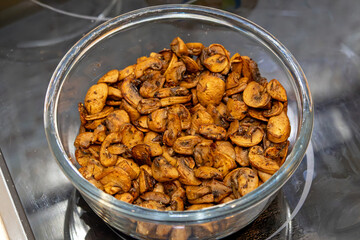 Brown baked fresh mushrooms cut in pieces inside glass bowl in kitchen