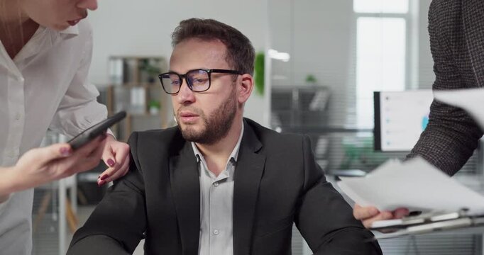 Businessman manager in office under stress overload. Colleagues thrust paperwork and demand decisions as the man navigates multitasking and deadline pressure. Severe stress and tight deadlines.