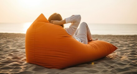 Woman relaxing in orange beanbag on beach at sunset, facing away