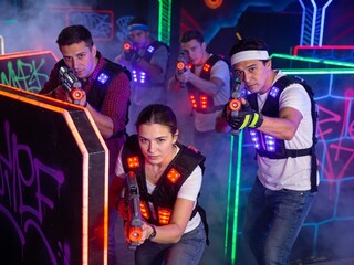 Fototapeta premium Young adults playing laser tag in futuristic arena with colorful neon lighting and fog. Teamwork and fun in modern recreational activity.