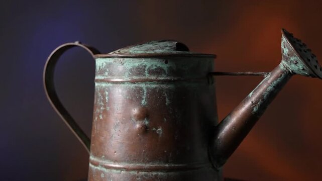 A captivating close-up showcases a vintage copper watering can, richly adorned with beautiful green and blue verdigris patina. The distressed metal surface tells a story of time and use, highlighting 