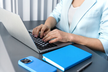 Female administrator typing on laptop at the desk. Daily work tasks, business routine, productivity and organized workspace. Selective focus.