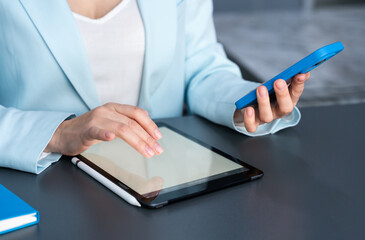 A female administrator uses a smartphone and tablet at her office workstation. Communication, documentation, administrative work routine. Selective focus.