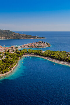 Aerial view of the peninsula's terracotta rooftops meet the azure Adriatic, fringed by verdant pines, a tapestry of Croatian coastal charm, Primosten, Sibenik-Knin County, Croatia.