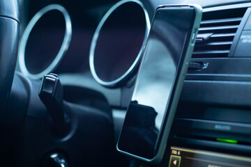 A close-up of a phone attached to a car's dashboard. The dashboard features green-lit controls and buttons.