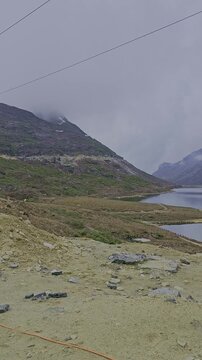 Vertical panning shot of Sela Lake at Sela Pass in April. Crystal clear high altitude water with black rocky mountains, snow patches, and dramatic white clouds. 4K Samsung S23 Ultra.