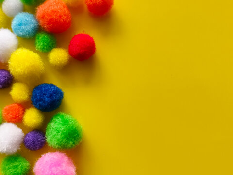 Fluffy, colorful pom-poms set against a bright yellow background are perfect for DIY art projects.
