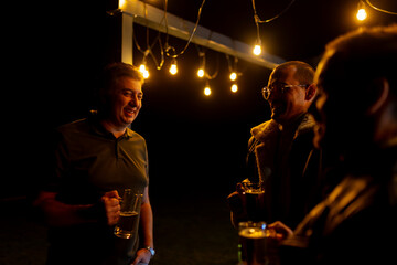 Obraz premium Group of cheerful friends enjoying a social evening outdoors under warm lighting