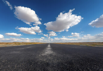 Empty asphalt road with strong leading lines under bright blue sky and fluffy white clouds. Open landscape background representing travel, freedom, journey, transportation.
