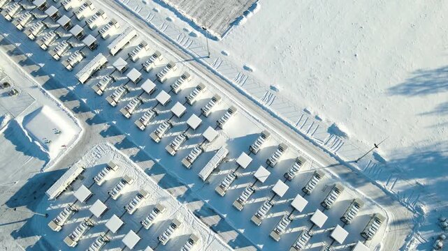 Top-down aerial view of a large utility scale battery energy storage facility in winter, slowly pulling back and rotating to reveal containerized storage units, grid infrastructure, and snow-covered l