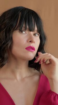 Caucasian Woman In Pink Dress Posing Contemplatively, Intimate Studio Portrait With Bob Haircut And Bangs, Magenta Lipstick And Matching Manicure, Soft Warm Backdrop, Subtle Head Turns And Thoughtful
