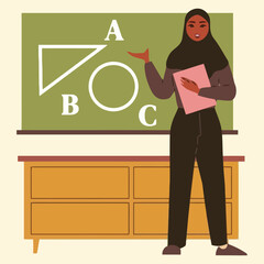 A Muslim woman teacher in a hijab stands in front of a chalkboard with geometric shapes and letters, holding a book.