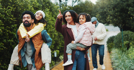 Family, children and walk at park, happy and piggy back with point for sightseeing, holiday and bonding. People, parents and grandparents with kids, vacation or outdoor together at urban garden