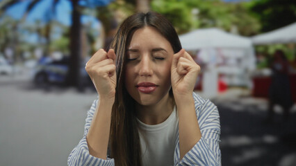 Naklejka premium Woman gently rubs her eyelids on a busy city street with white canopy stalls behind her; irritation.
