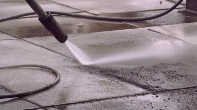 Pressure washer nozzle spraying water to clean a concrete driveway, removing dirt and grime,.