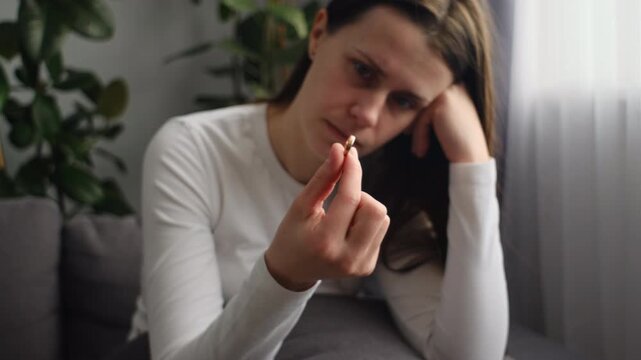 Worried sad young woman holding wedding ring. Divorcee going through depression, apathy, heartbreak crisis. New widow feeling emotional pain, grieving after loss