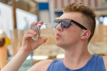 young man is drinking a glass of beer while wearing sunglasses
