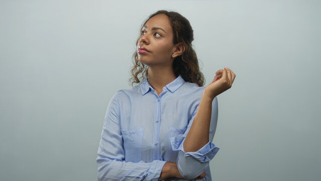 Woman with raised hand and folded arm posing in studio against pale blue wall; thoughtful reflection.