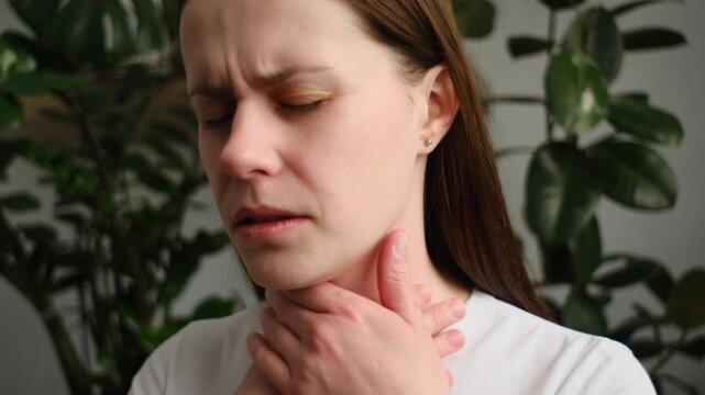 Sad female suffering from pain sitting on sofa at home. Healthcare and medical concept. Unhealthy sad young caucasian woman with sore throat inflamed tonsils from influenza symptoms