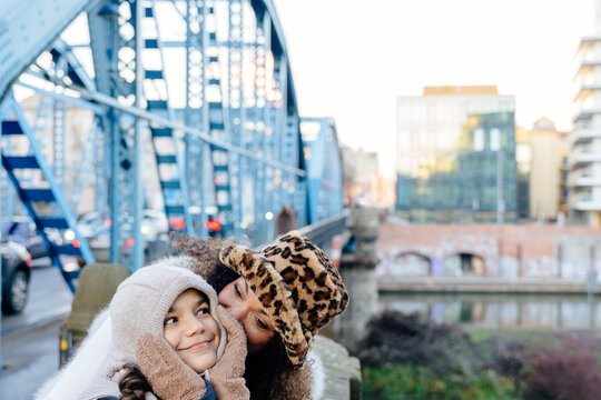Happy mother in leopard print hat whispering to her teen daughter, family love and secret