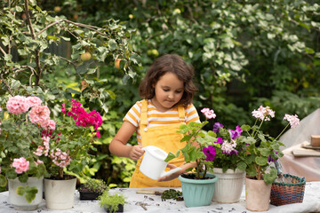 A young kid girl in yellow overalls tends to potted plants in a lush garden