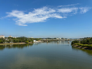 Obraz premium PUTRAJAYA, MALAYSIA - FEBRUARY 4, 2026: A wide panoramic view of Putrajaya Lake featuring the Seri Bakti Bridge, lush greenery, and a clear blue sky with wispy clouds during a calm morning.