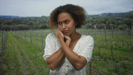 Fototapeta premium Woman with hand on cheek in a vineyard field, crossing arms and wincing in pain for toothache; distress toothache worry.