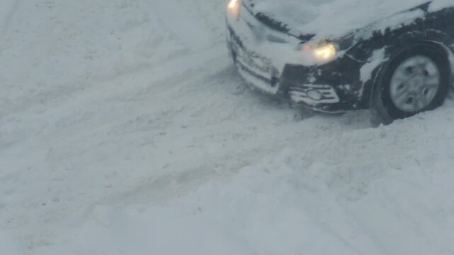 Car front stuck in deep snow. Headlights on. Front wheel spins. No traction. Vehicle struggles to move. Challenging winter driving conditions. Transportation issue.