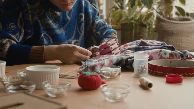 Low angle shot of unrecognizable woman with prosthetic arm using needle and thread to patch shirt in thrift store