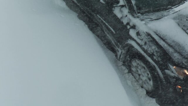 Automobile stuck and immobilised in extensive snowdrift on roadside, front portion with headlights visible through dense white snow