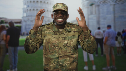 Soldier man in camouflage uniform with hands raised and smiling in front of building; pride duty...