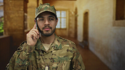 Man in camouflage uniform holding phone to ear with dogtags visible in building; duty and...